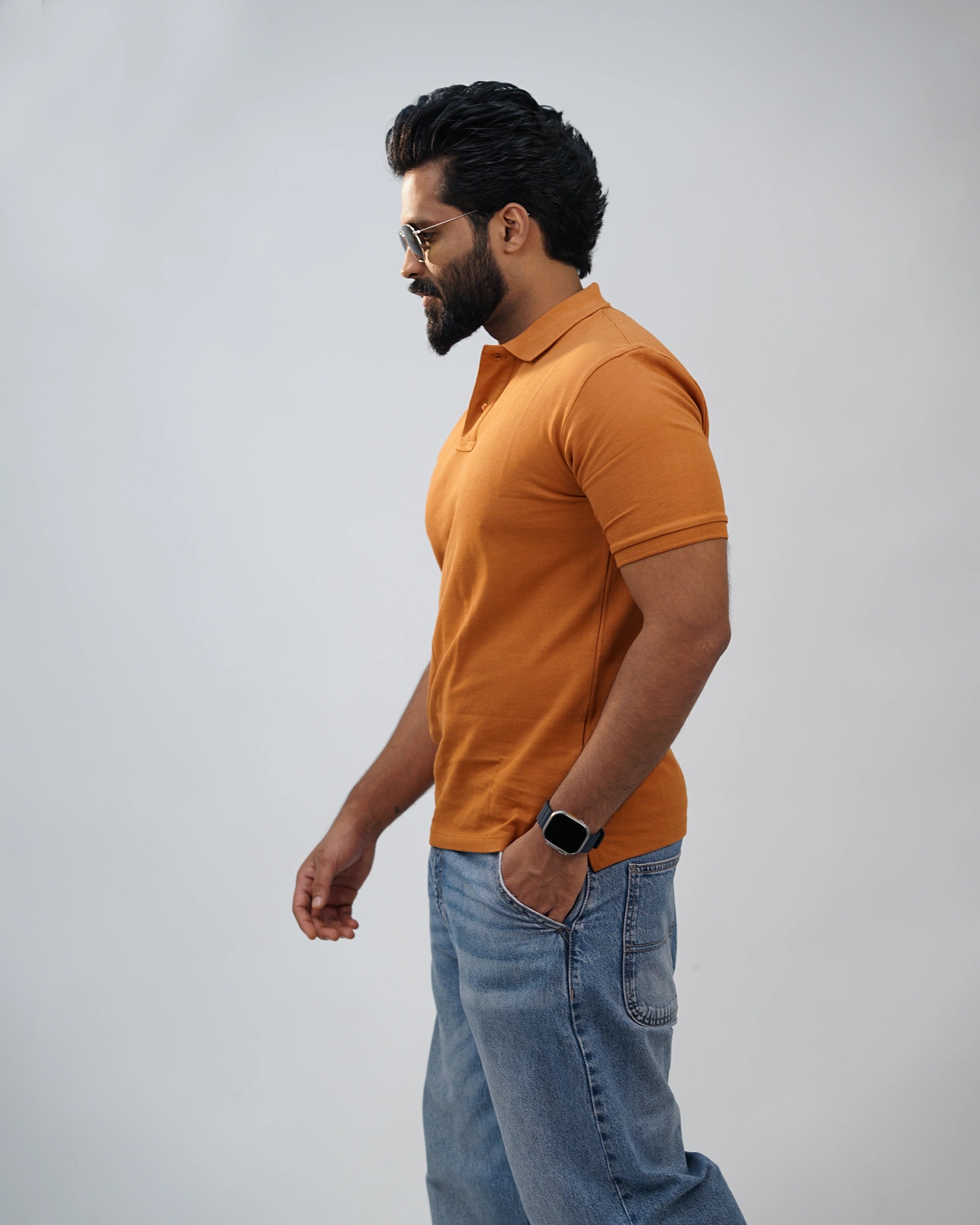 Model walks casually towards the camera with a confident smile, showing the natural fit of the tee in motion. Hands can be swinging naturally or one in the pocket.