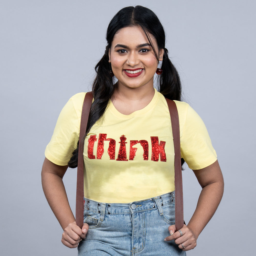 Yellow “Think” women’s tee with red glitter typography and crown – front view
