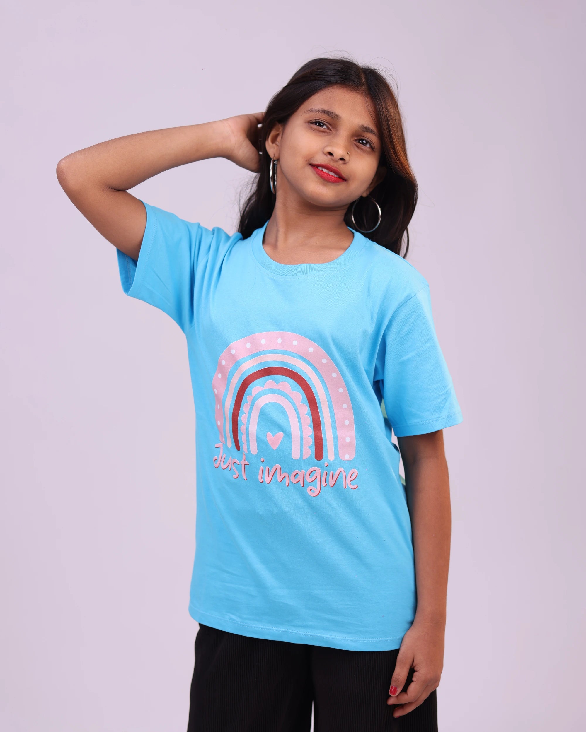 Child wearing “Just Imagine” tee, daydreaming in sky blue—casual, creative style