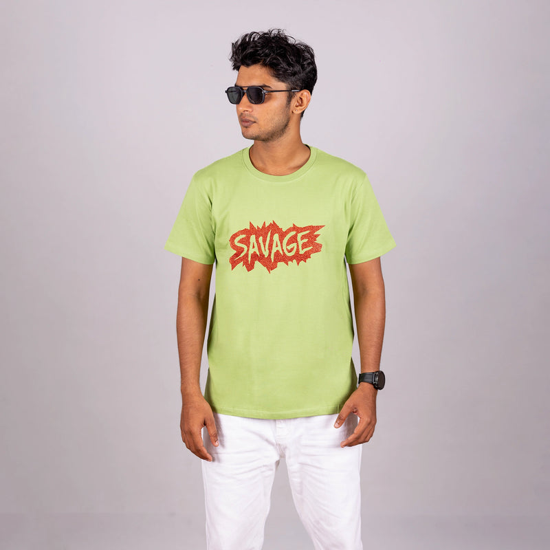 Man wearing kiwi green “Savage” tee with casual trousers—bold style with playful edge