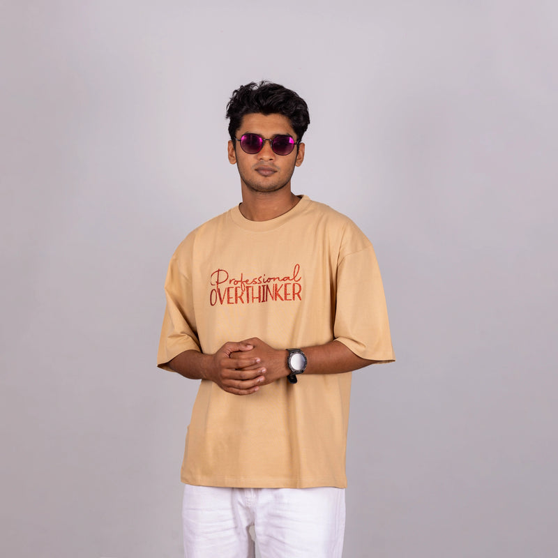 Man seated casually in “Professional Overthinker” tee—effortless mood, relaxed style moment